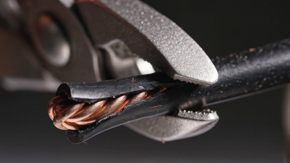 Extreme close-up of a wire stripper pulling black insulation off a stranded copper conductor